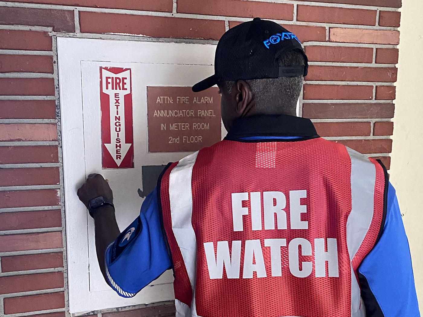 Foxtrot officer in a FIRE WATCH vest logging a round at a building fire alarm annunciator panel