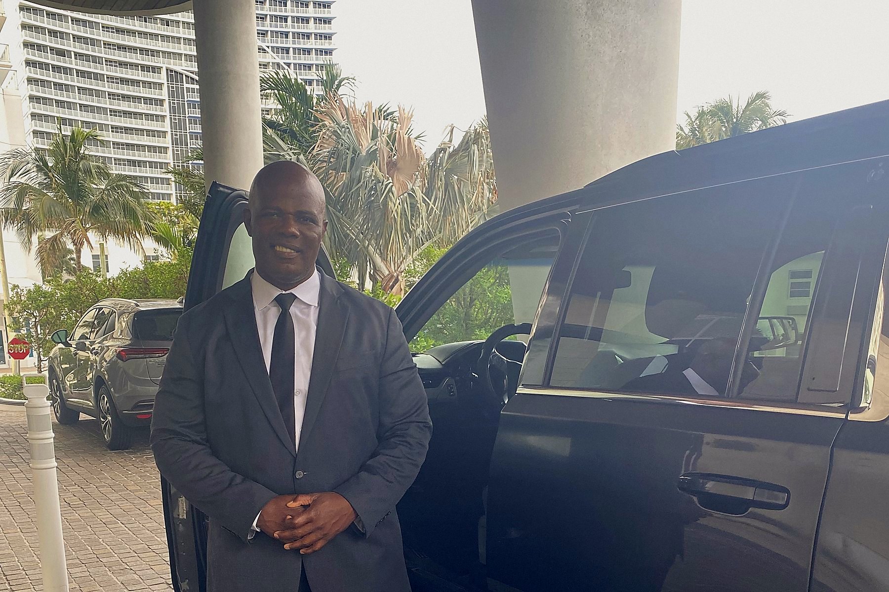 Foxtrot officer in a suit beside a black SUV at a South Florida residential tower